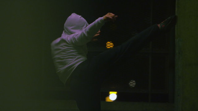 Hooded male fighter training at night in urban setting