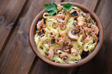 Tagliatelle with sliced octopuses in a ceramic bowl, studio shot