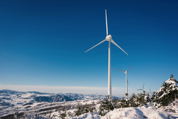 Wind turbines on snow winter landscape with dark blue sky.