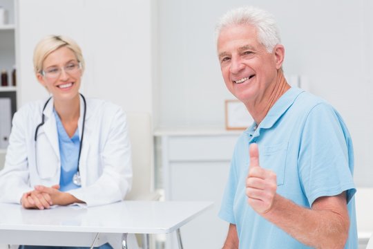 Senior patient gesturing thumbs up while doctor looking at him