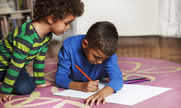 Young mixed race boys drawing on paper with crayon.