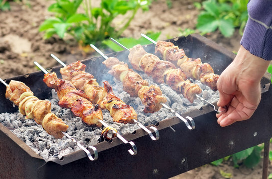 Man's hand turn over kebabs on a barbecue