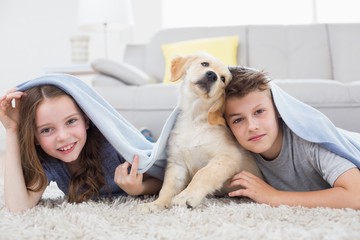 Cute siblings with dog under blanket in living room