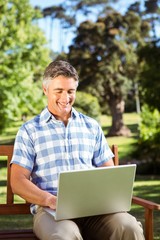 Fototapeta premium Man sitting on park bench using laptop