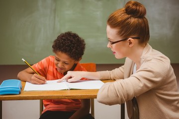 Teacher assisting little boy with homework in classroom