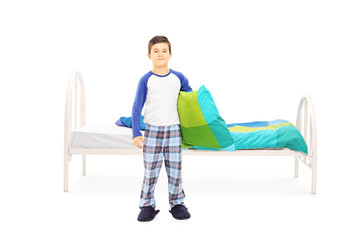 Little boy with pillow standing in front of a bed
