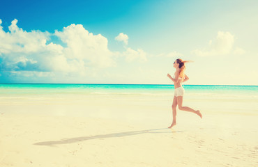 Young woman running on summer beach on coast of the ocean