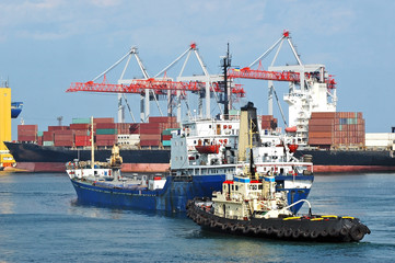Naklejka premium Tugboat assisting bulk cargo ship to harbor quayside