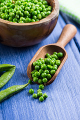 Wooden scoop with fresh peas on blue table