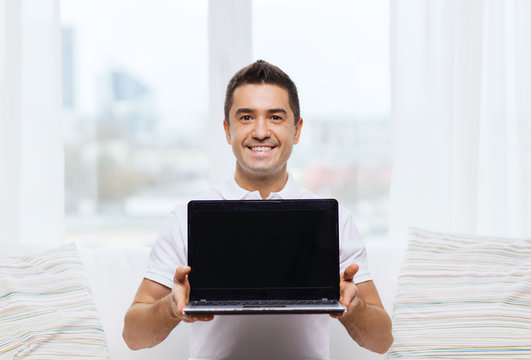 happy man showing laptop blank screen at home
