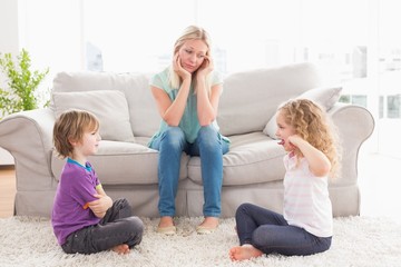 Upset mother looking at children fighting on rug