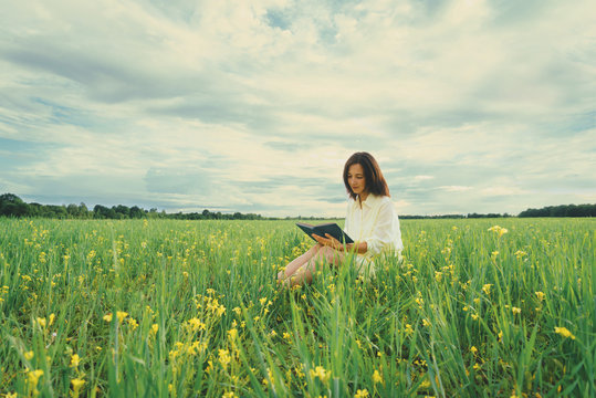Girl reading a book on summer wildflower meadow