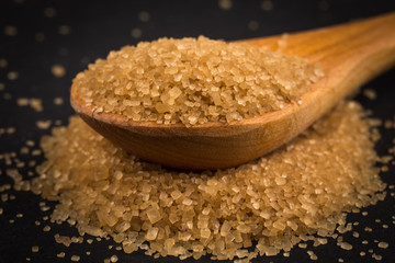 Brown sugar in wooden spoon on dark background