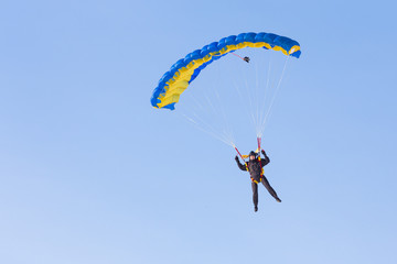 Skydiver on blue and yellow parachute on background blue sky