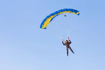 Poster Skydiver on blue and yellow parachute on background blue sky © Aleksei Lazukov