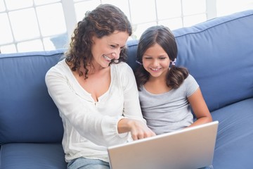 Happy mother and daughter sitting on the couch and using laptop