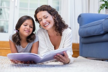 Happy mother and daughter lying on the floor and reading a book