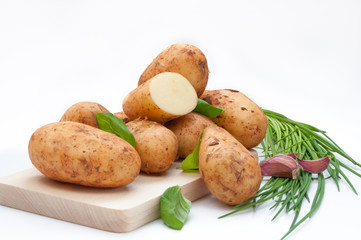 Potatoes on wooden board with basil, garlic, spring onion