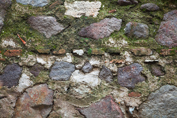 Old wall made of dark gray stones with green moss
