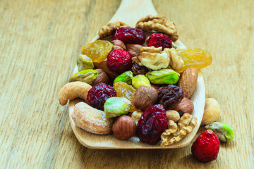 Varieties of dried fruits and nuts on wooden spoon.