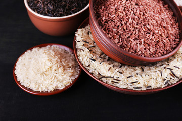 Different kinds of rice in bowls on wooden background