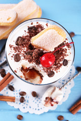 Tasty tiramisu dessert in glass, on color wooden background