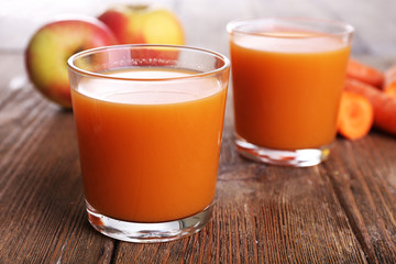 Glasses of juice with apple and carrot on wooden table close up