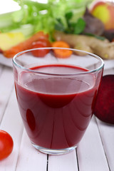 Glass of beet juice with vegetables on wooden table closeup