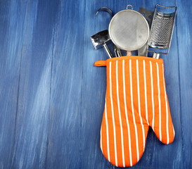 Different kitchen utensils in potholder on wooden background
