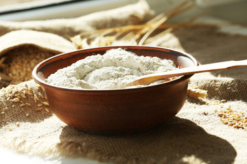 Bowl of flour with wooden spoon on burlap cloth background