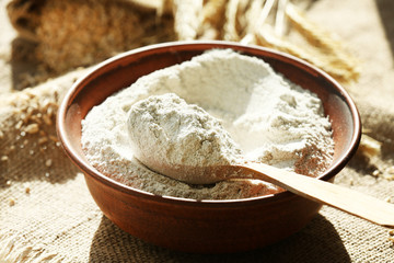 Bowl of flour with wooden spoon on burlap cloth background