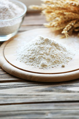Fototapeta na wymiar Pile of flour on cutting board with glass bowl, closeup