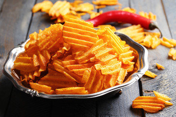 Delicious potato chips on plate on wooden table close-up