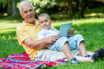 Naklejka na ściany i meble grandfather and child in park using tablet