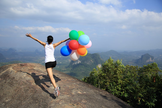 young asian woman mountain peak  running with colored balloons 