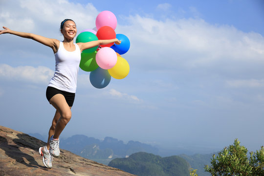 young asian woman mountain peak  running with colored balloons 