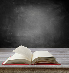 Open pages book on table in front of blackboard in classroom. Copy space