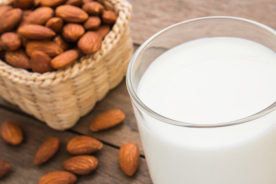 Almond milk in glass with almonds on wooden table