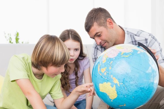 Children exploring globe while sitting with father