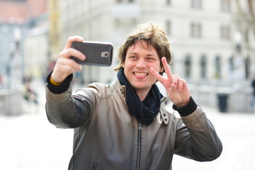 Young handsome hipster man making funny selfie in the city