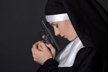 young woman nun praying with gun over grey