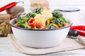 Frozen vegetables in bowl on napkin, on wooden table background