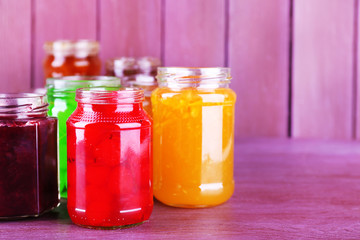 Homemade jars of fruits jam on color wooden background