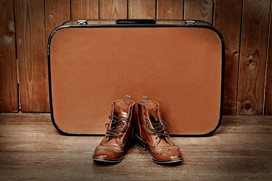 Retro suitcase with male shoes on wooden wall background