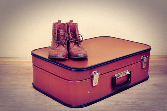 Vintage suitcase with male shoes on  floor on wall background