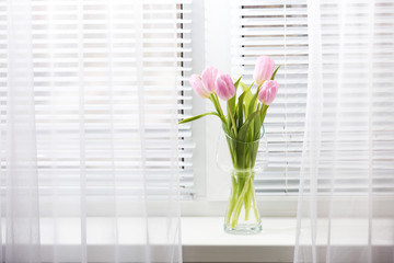 Beautiful pink tulips in glass vase on windowsill background