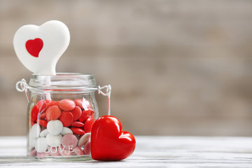 Sweet candies in glass jar with hearts on wooden background