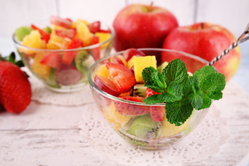 Fruit salad with mint in glassware on color wooden background