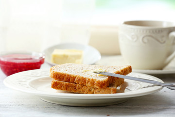 Toasts with butter on plate with cup of tea on light background