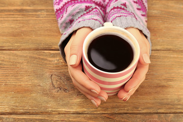 Fototapeta na wymiar Female hands holding cup of coffee on wooden background